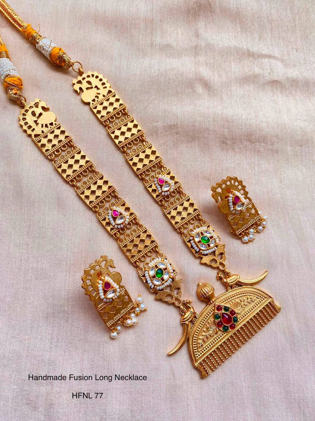 A long gold-tone necklace with geometric lattice links, peacock motifs and a broad fringed pendant.