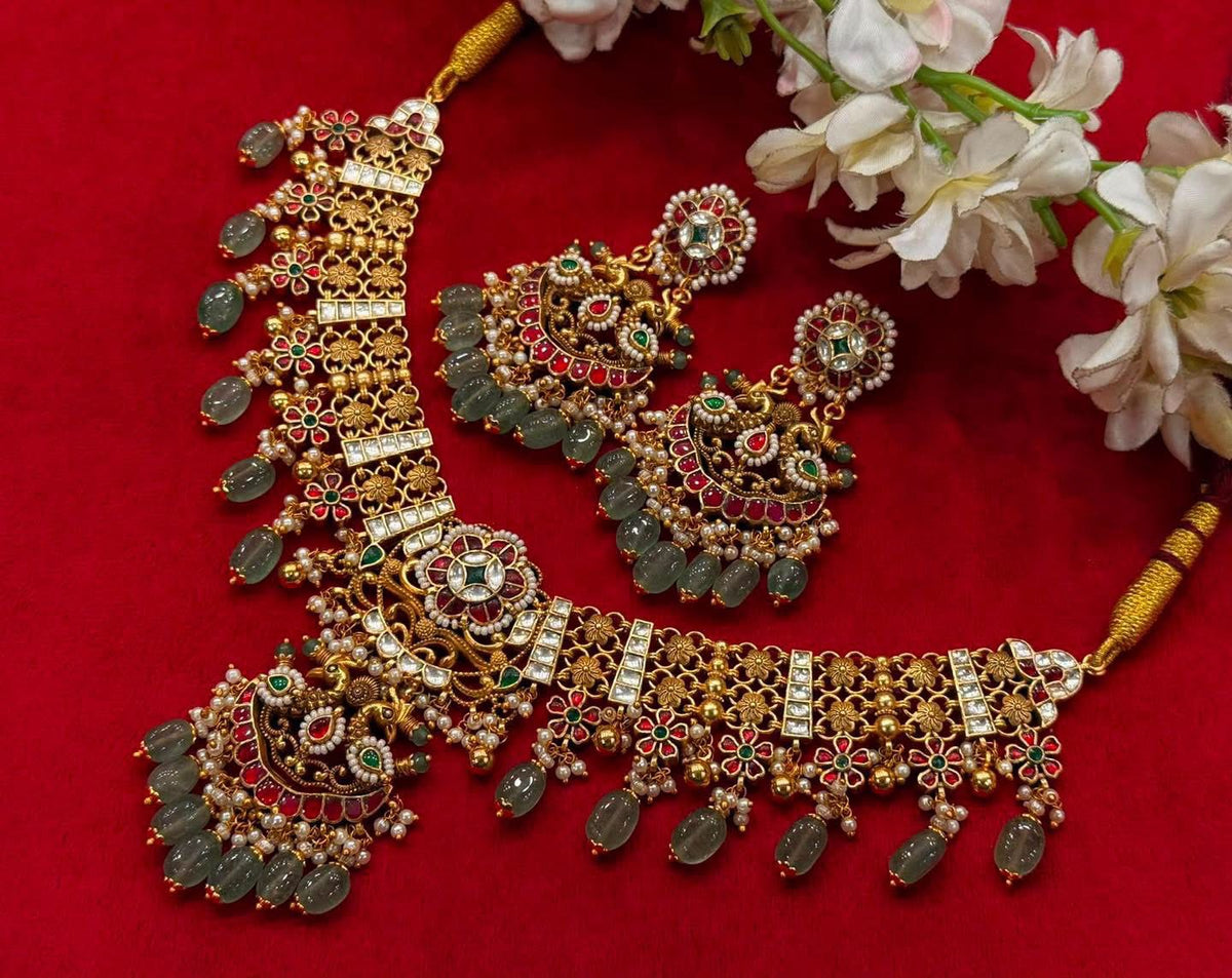 A broad floral necklace with red, green and clear accents, an ornate pendant and pale green drops.